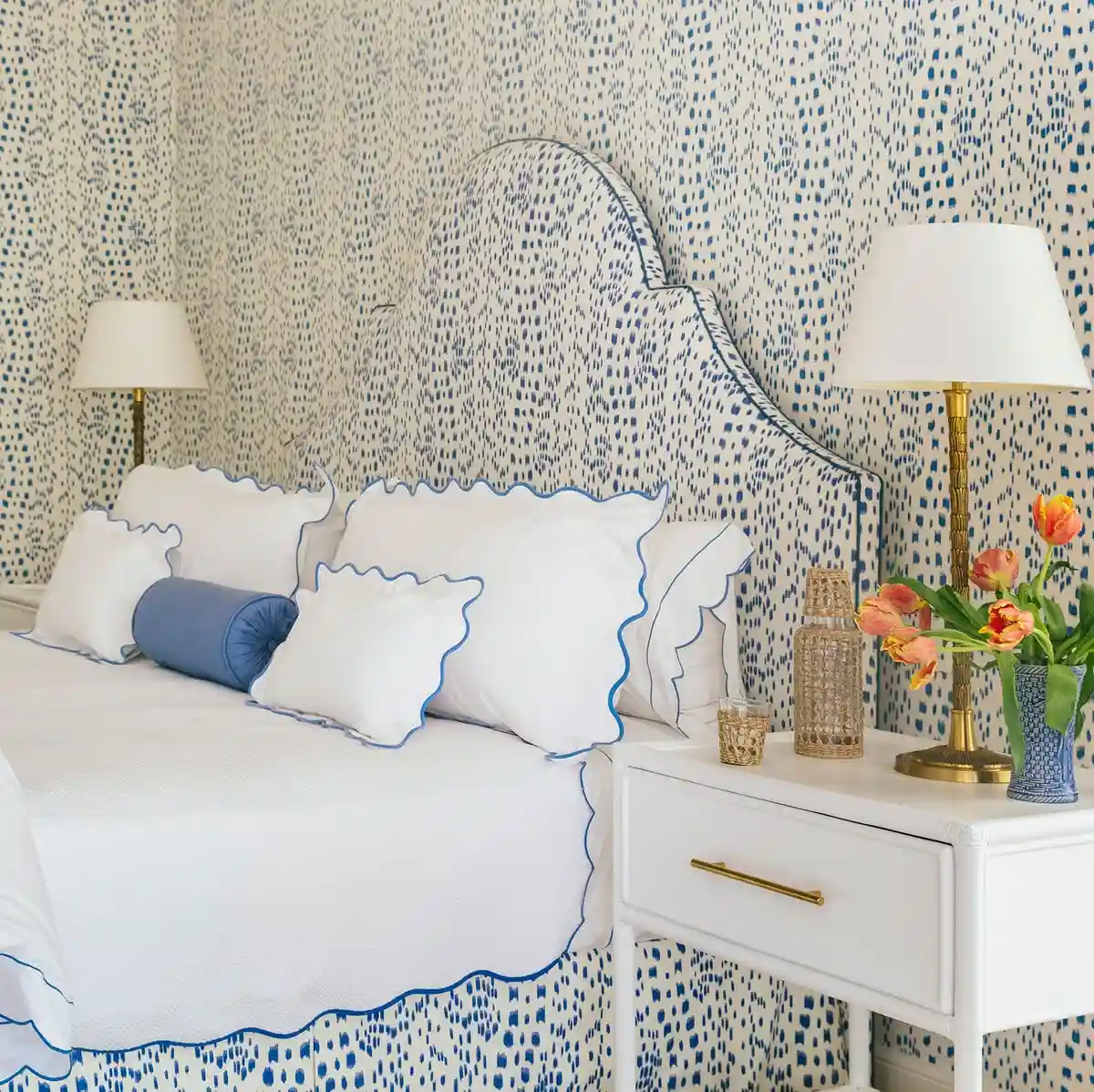 Bedroom with a white bed, blue-trimmed pillows, white nightstand, and blue-speckled wallcovering.