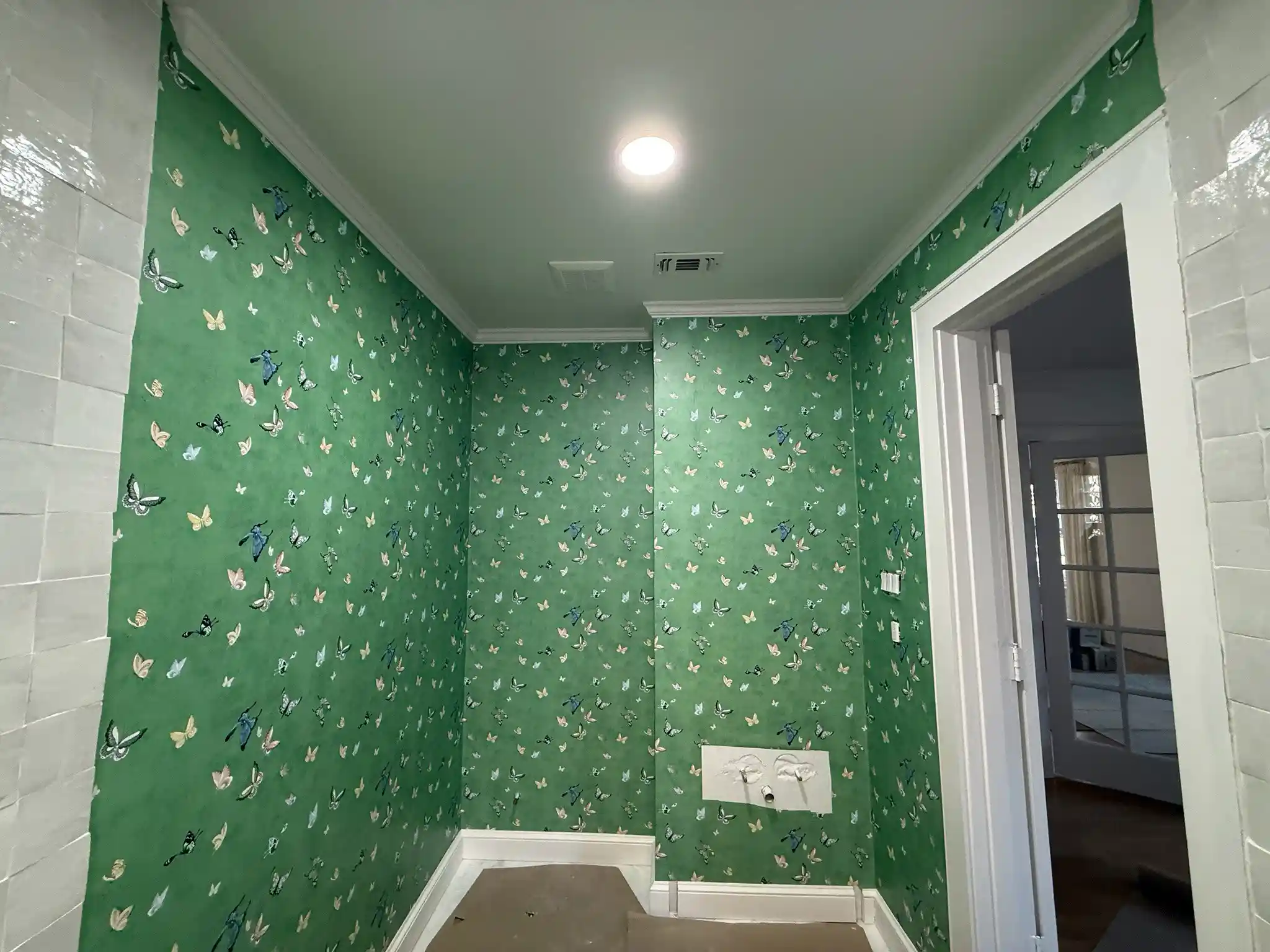 Small bathroom with green butterfly-patterned wallcovering, white tile, and a doorway.